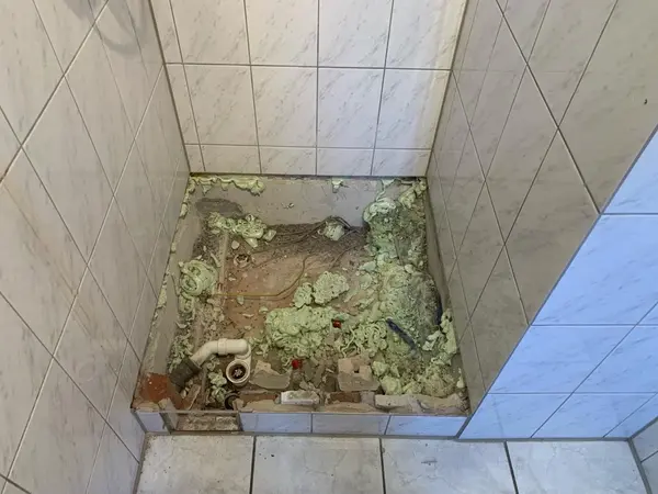 Duschbereich im Bad mit freiliegenden Rohren, Bauschaum und fehlender Duschwanne.
