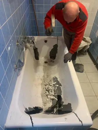 Handwerker entfernt alte Beschichtung von beschädigter Badewanne zur Renovierung im Badezimmer.