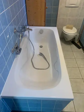 Weiße Badewanne mit Handbrause, blauen Fliesen und moderner Toilette im Badezimmer.