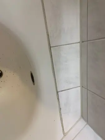 Weiße Badfliesen mit schiefer Fuge an einer Badewanne, leichte Verschmutzung sichtbar.