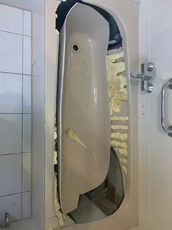 Beschädigte Badewanne im Badezimmer mit aufgerissener Wanne und sichtbarer Isolierung.