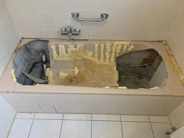 Badewanne mit herausgeschnittenen Öffnungen zur Renovierung und sichtbaren Rohrleitungen